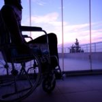 man in wheelchair in front of large windows